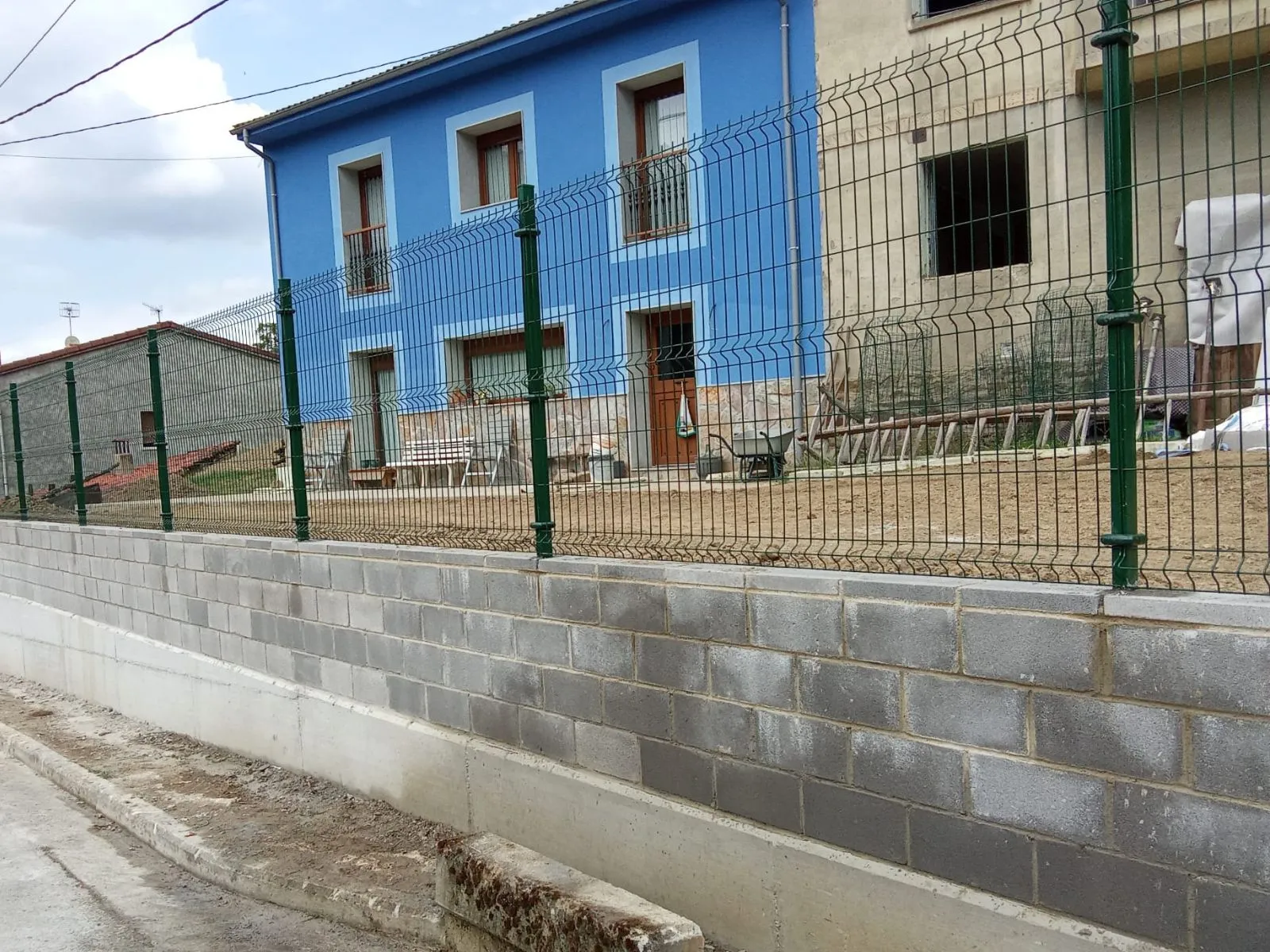 Cerramiento de finca con muro de bloques de hormigón y panel metálico rígido verde adaptado al desnivel del terreno.