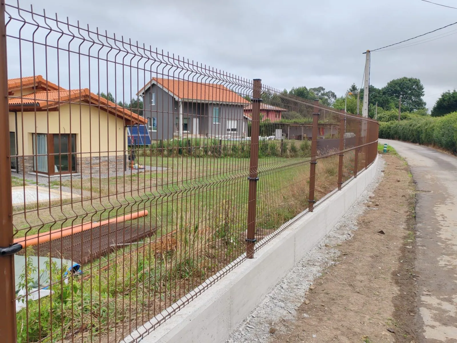 Cerramiento perimetral de parcela residencial con panel metálico rígido marrón instalado sobre un murete de hormigón.
