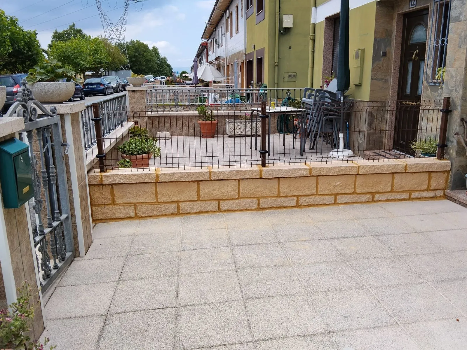 Cerramiento de patio delantero con murete de bloques decorativos y panel metálico rígido marrón en una vivienda.